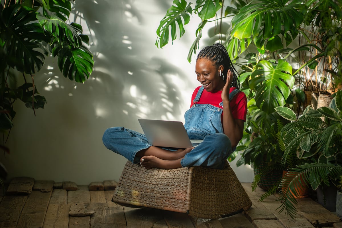 Woman on a laptop video call, sitting cross-legged among houseplants, showing how co-hosting can be run remotely