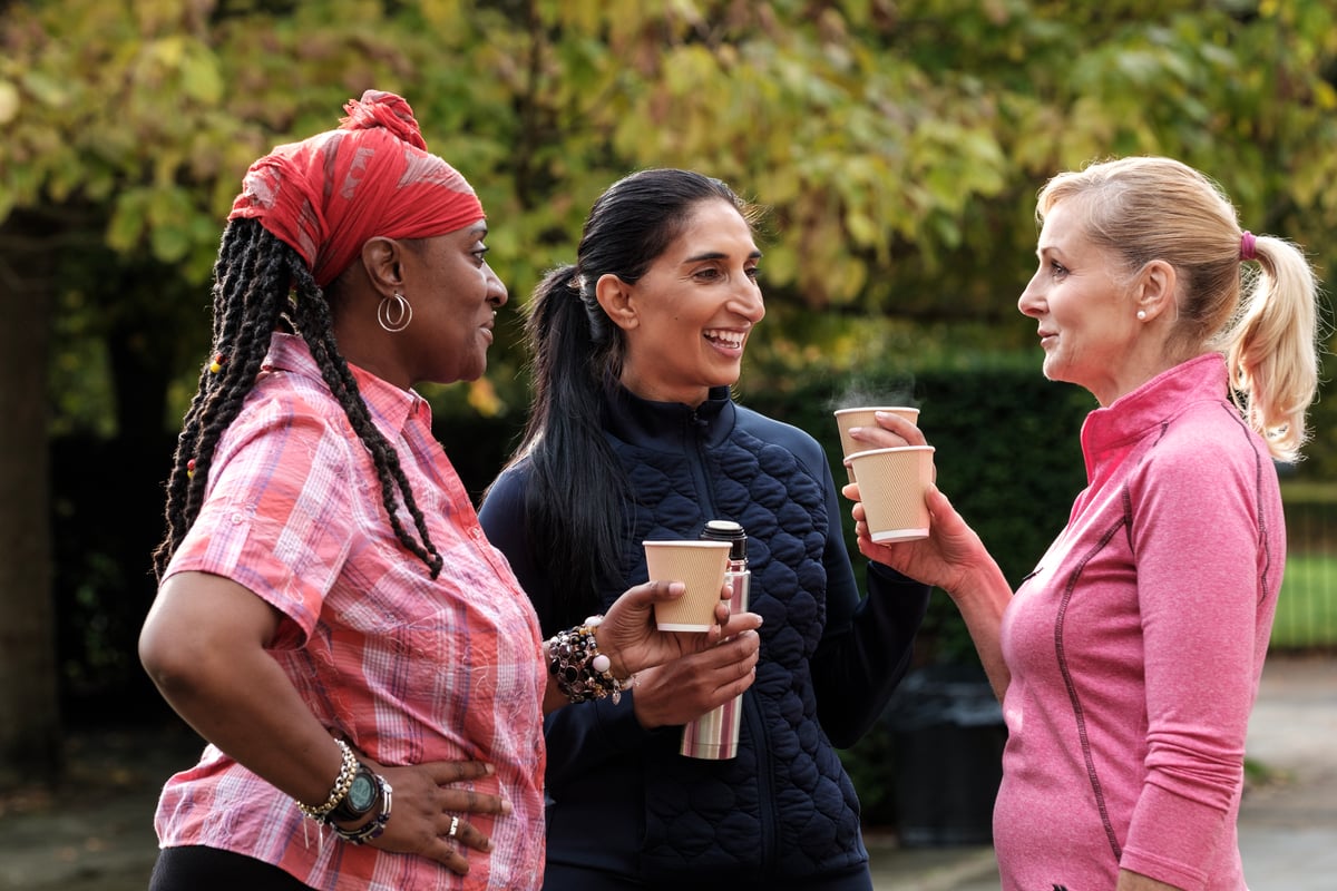 Three people chatting over takeaway coffee outdoors, networking to find first co-hosting clients